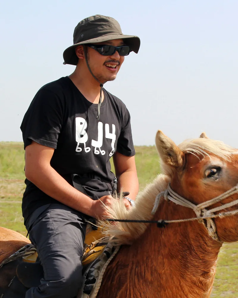 Joe on horseback on the grasslands, laughing.